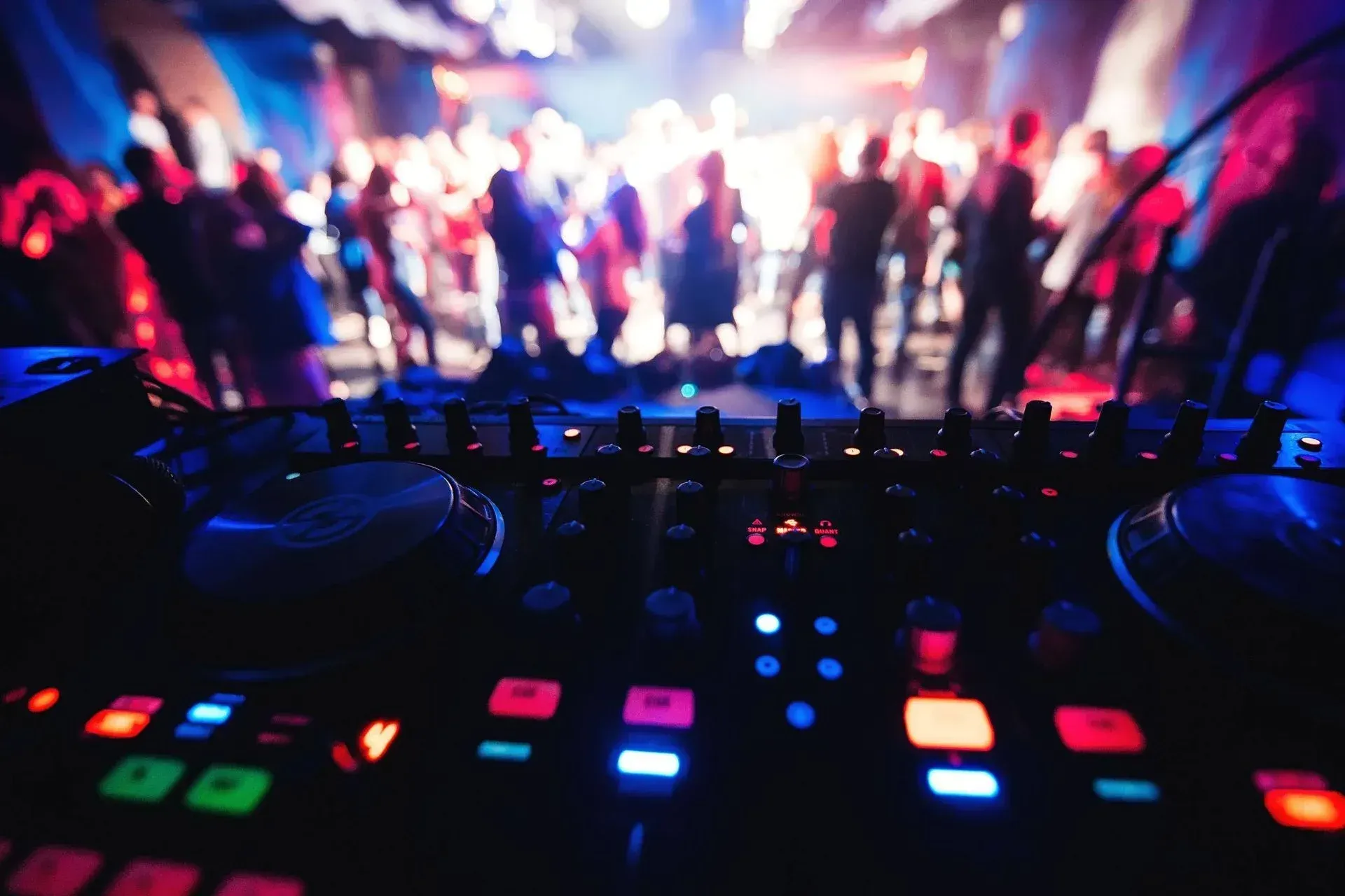 Un DJ está tocando música en una fiesta con una multitud de gente bailando de fondo.