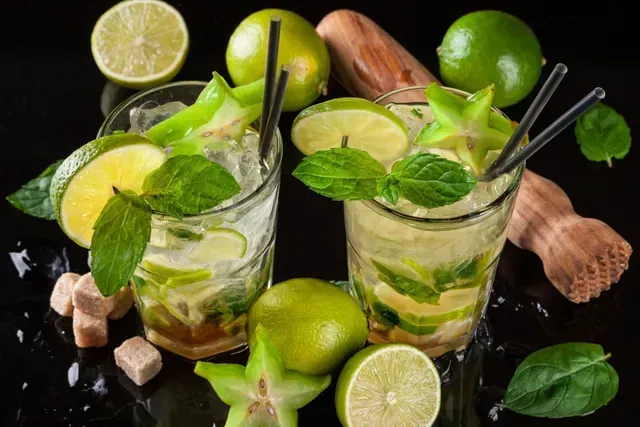 Dos vasos de mojito con pajitas y limas en una mesa.