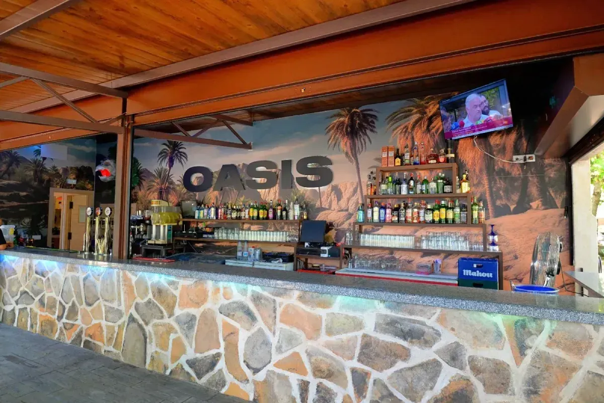 Un bar al aire libre con una barra de piedra, estantes con botellas y un mural con la palabra 