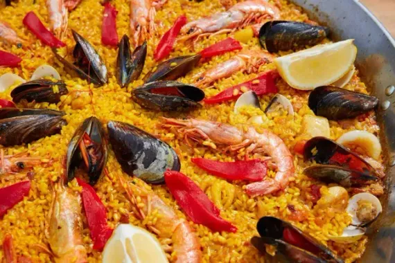 Una paella con gambas, mejillones, pimientos y rodajas de limón.
