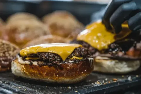 Una persona está poniendo queso en una hamburguesa sobre un pan.