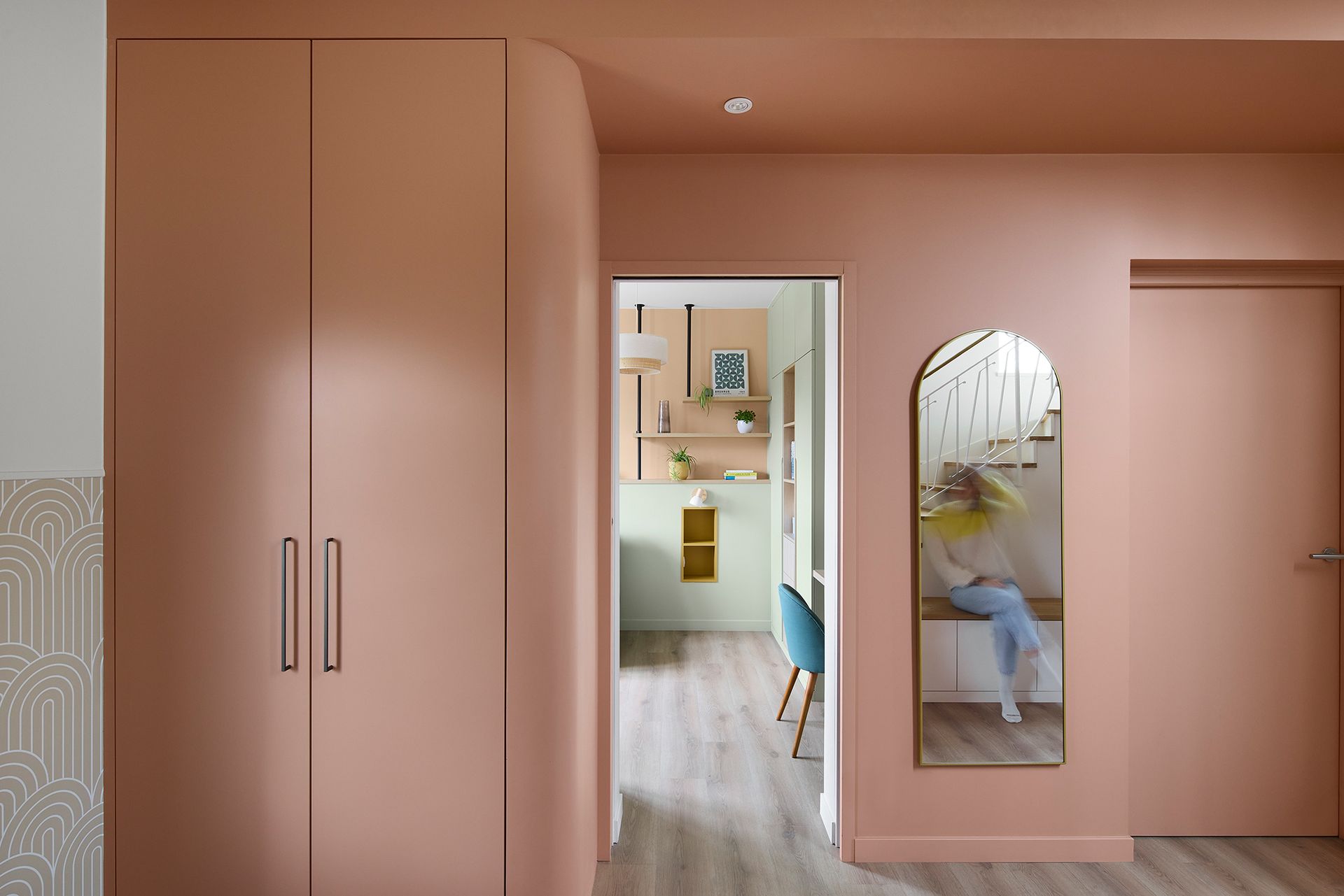 Couloir rose avec placards intégrés, porte donnant sur une cuisine et miroir mural.