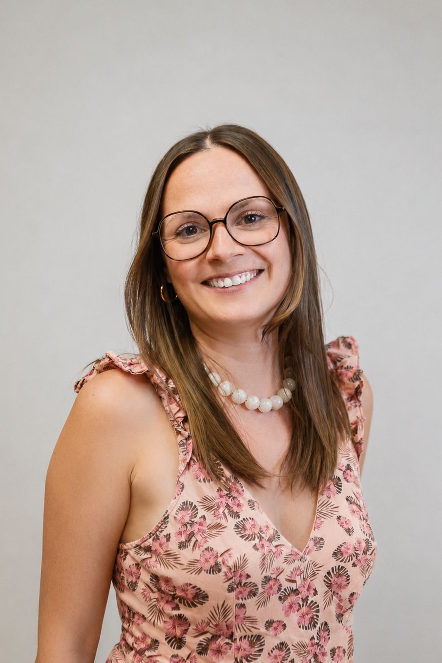 Femme souriante en blazer, debout à l'intérieur à côté de fleurs décoratives en papier.