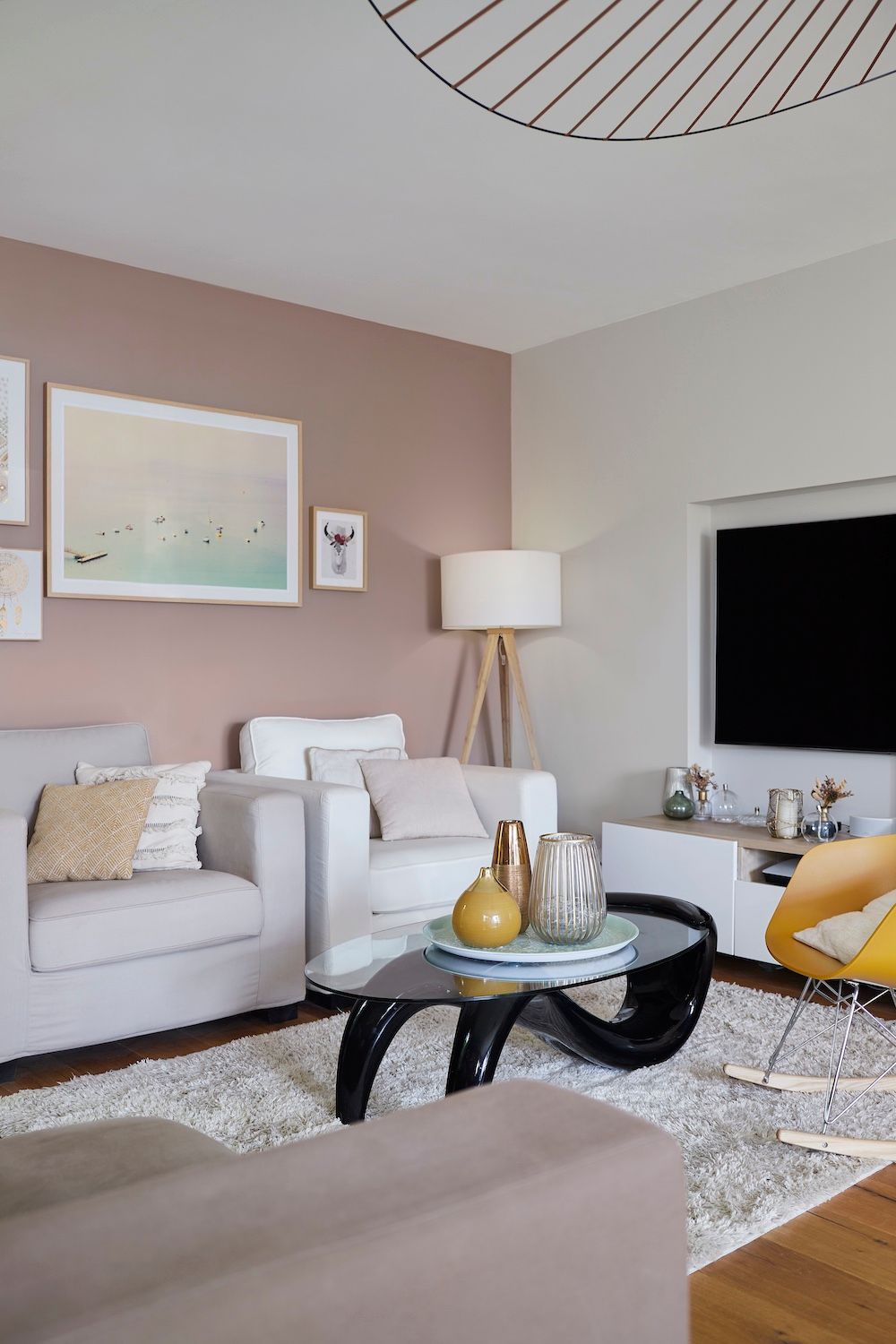 Salon moderne avec canapé beige, fauteuil blanc, table basse noire, lampe et grande télévision sur la droite.