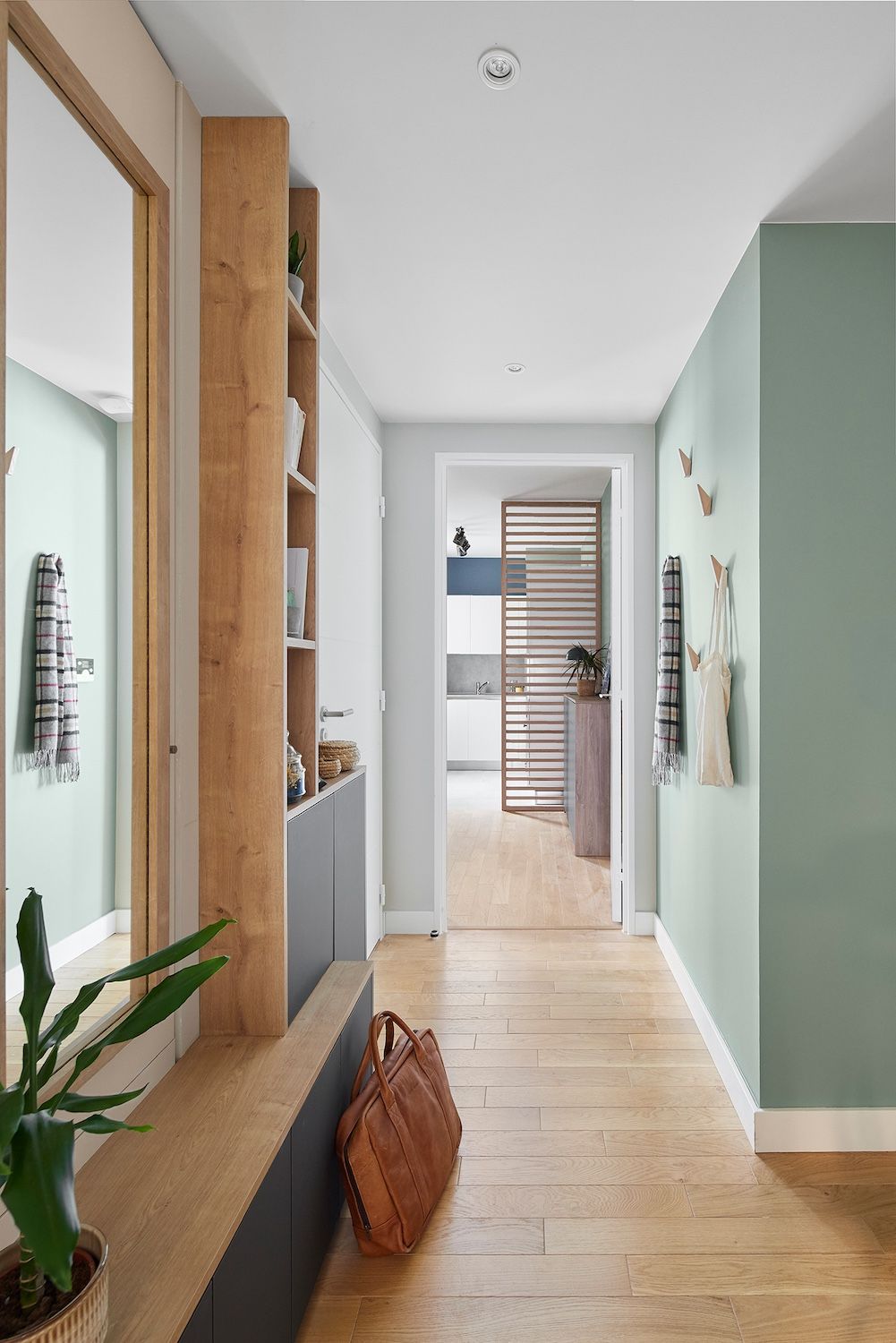 Couloir lumineux avec parquet, murs vert menthe, plantes et un panier près d'une porte ouverte.