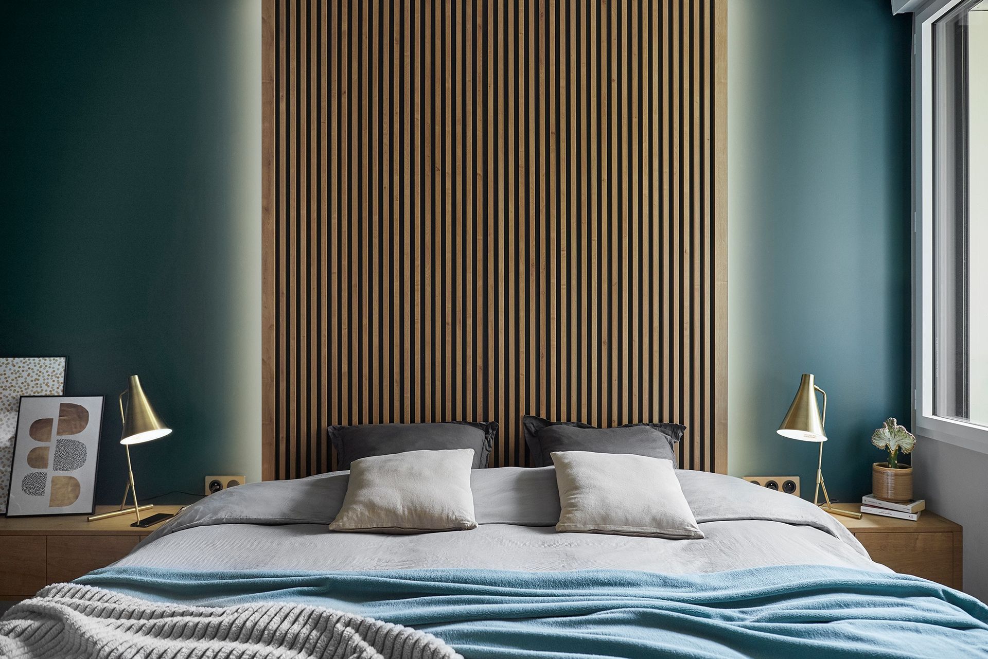 Chambre moderne avec une tête de lit en bois rayé, des murs bleu sarcelle et un lit soigneusement fait avec des oreillers gris.