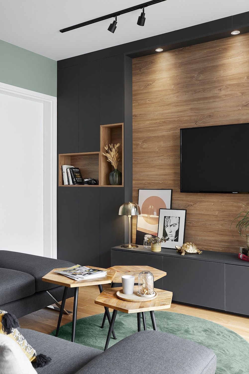 Salon moderne avec mur TV sombre, lambris, canapé noir et table basse ronde.