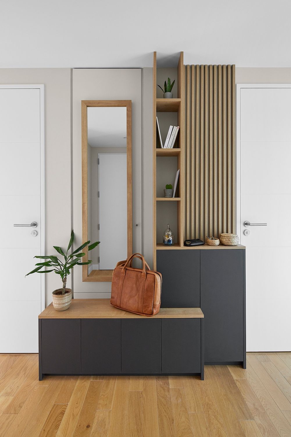 Entrée moderne avec banc en bois, miroir, plante et armoire de rangement noire sur fond de murs blancs.