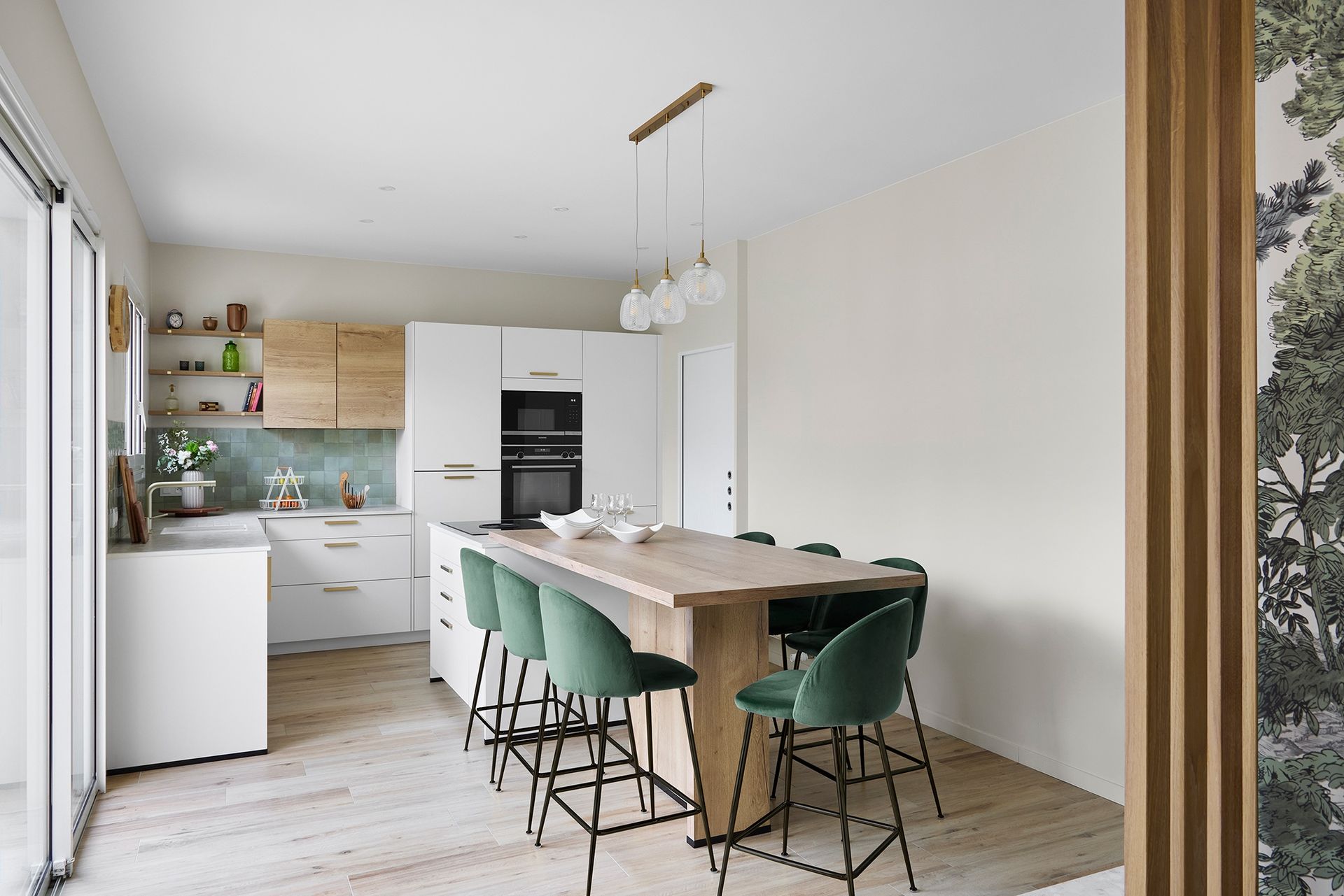 Cuisine-salle à manger lumineuse et minimaliste avec une table en bois, des chaises vertes et des placards blancs.