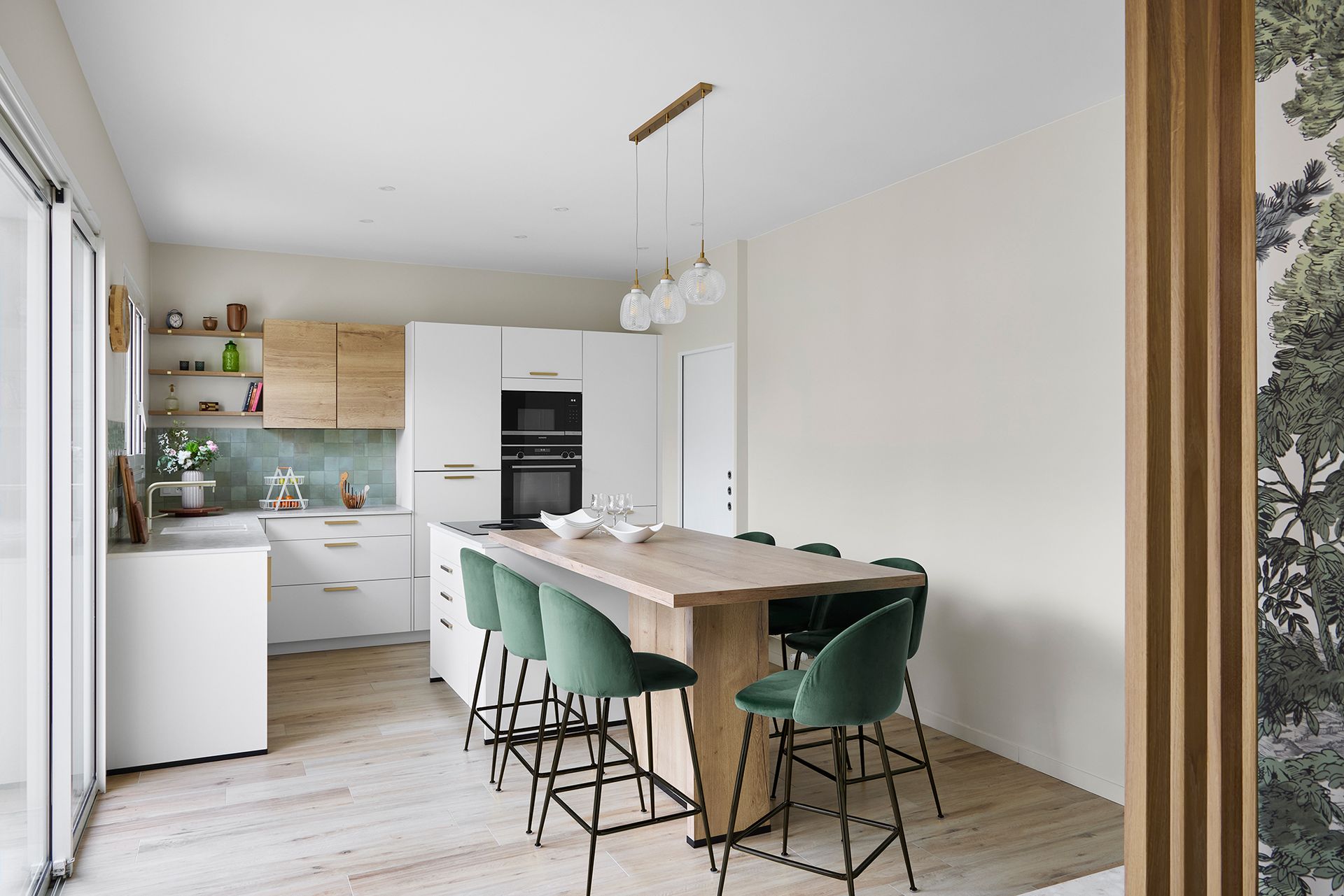 Cuisine moderne et lumineuse avec placards blancs, table à manger en bois et chaises vertes près d'une porte coulissante en verre