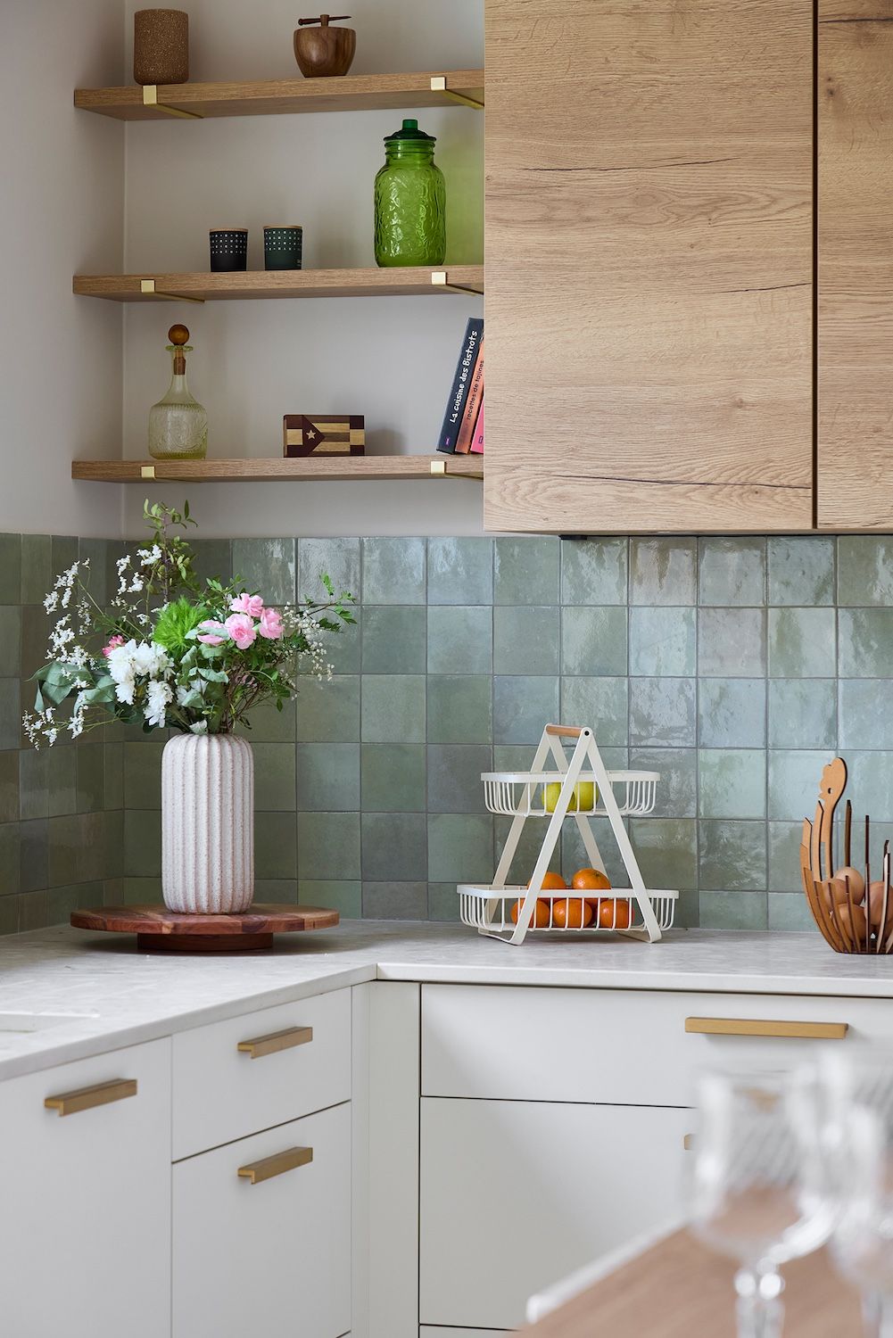 Coin cuisine moderne avec placards blancs, étagères en bois, crédence en carrelage vert et fleurs sur le plan de travail