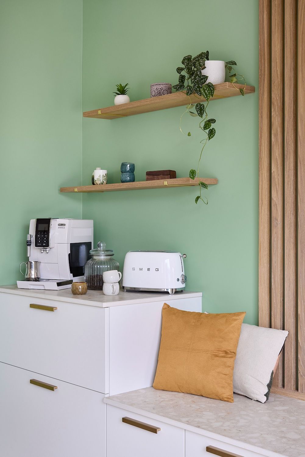 Kitchenette vert menthe avec placards blancs, étagères, cafetière, grille-pain et banquette avec coussins moutarde et blancs.