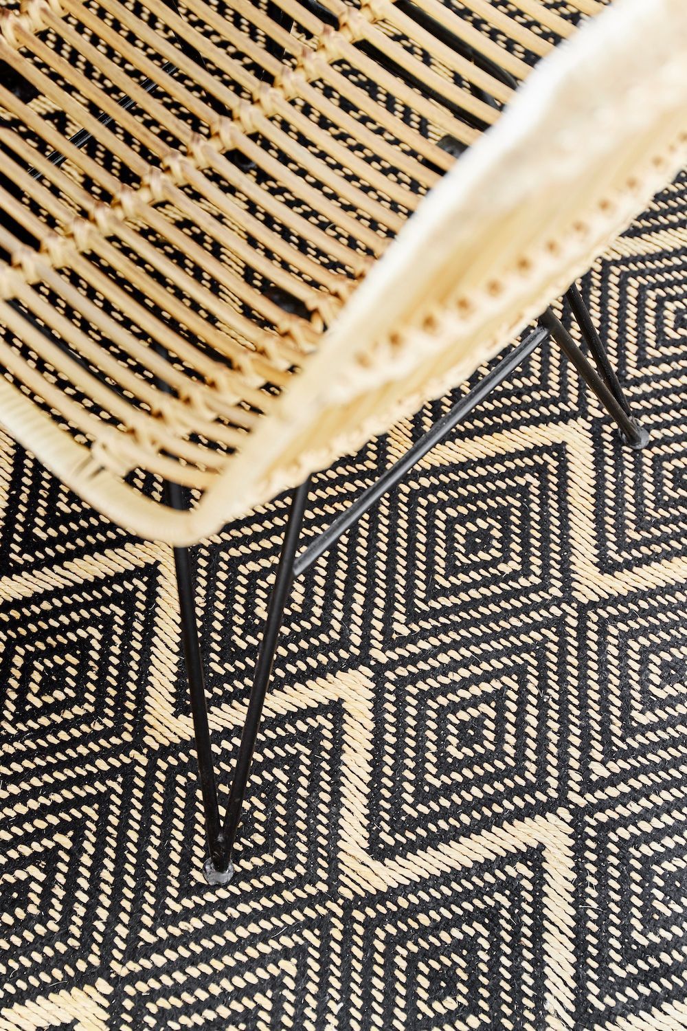 Une chaise tressée sur un tapis à motifs géométriques noirs et crème.