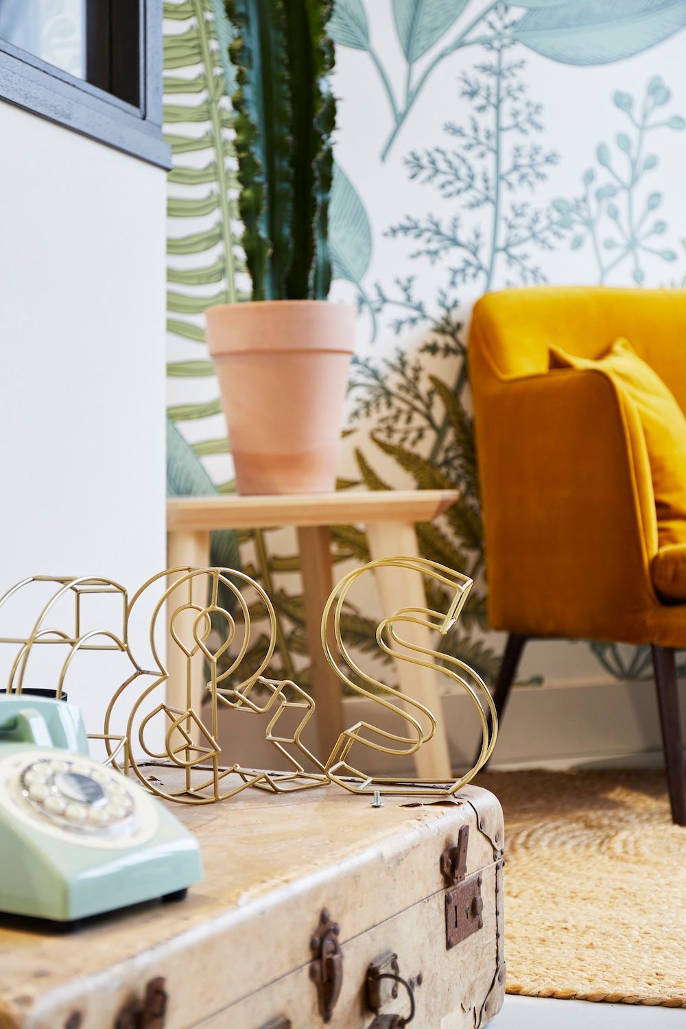 Salon cosy avec canapé moutarde, cactus en pot, papier peint et commode vintage à la décoration dorée