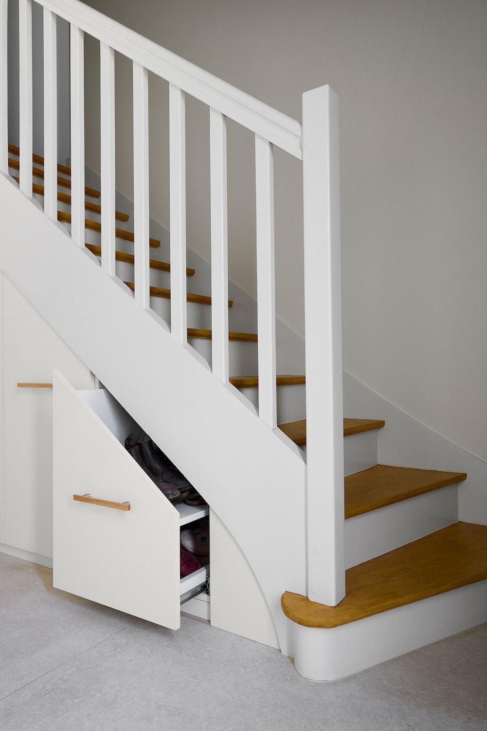 Escalier blanc avec marches en bois et petite porte de rangement sous l'escalier dans un intérieur recouvert de moquette