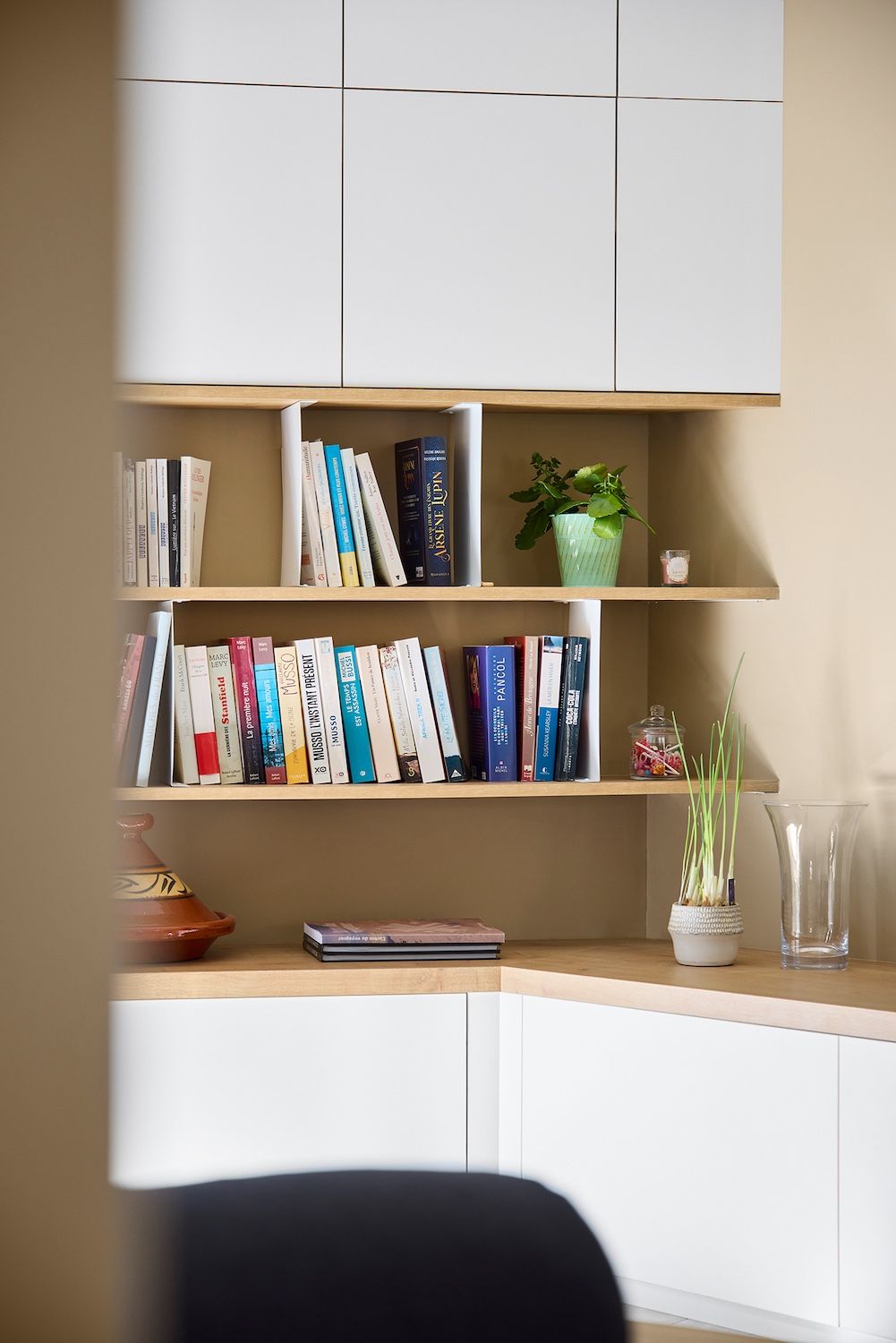 Des placards blancs intégrés et des étagères en bois avec des livres et des plantes dans un coin cosy