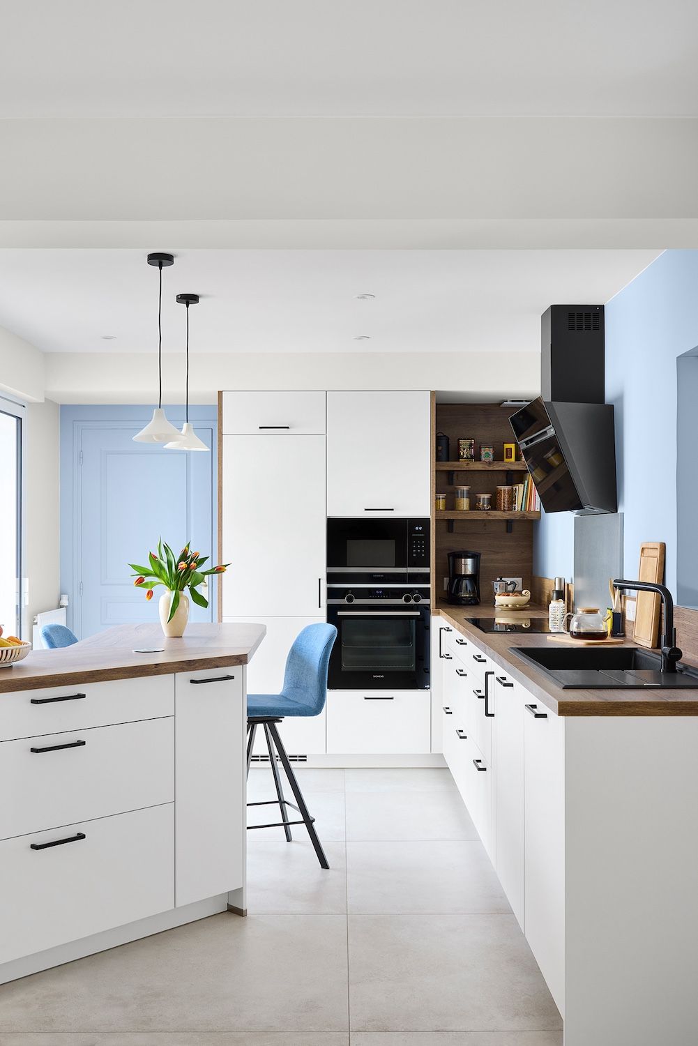 Cuisine moderne et lumineuse avec armoires blanches, îlot central, tabourets bleus et comptoirs noirs.