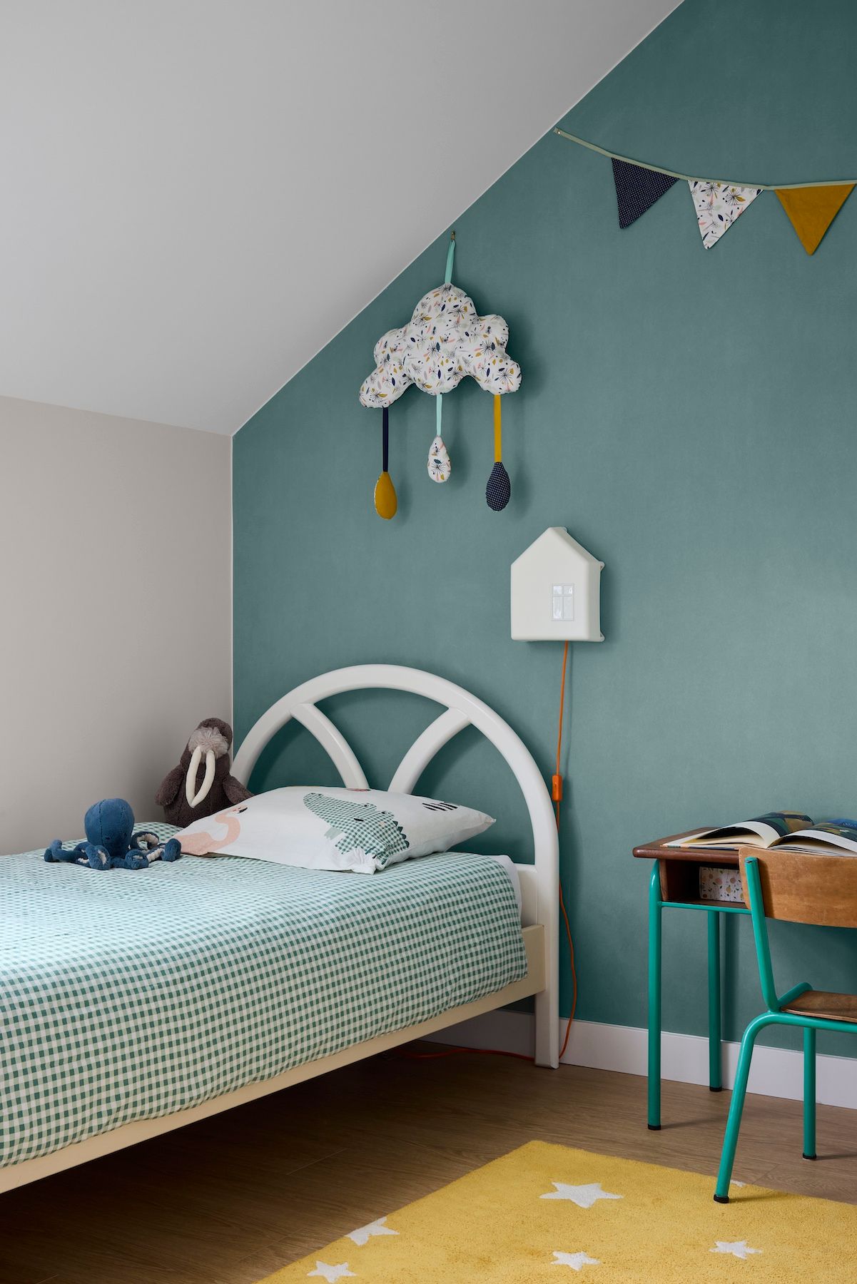 Chambre confortable aux tons turquoise, avec lit blanc, décoration murale nuageuse et petit bureau sous le plafond mansardé.