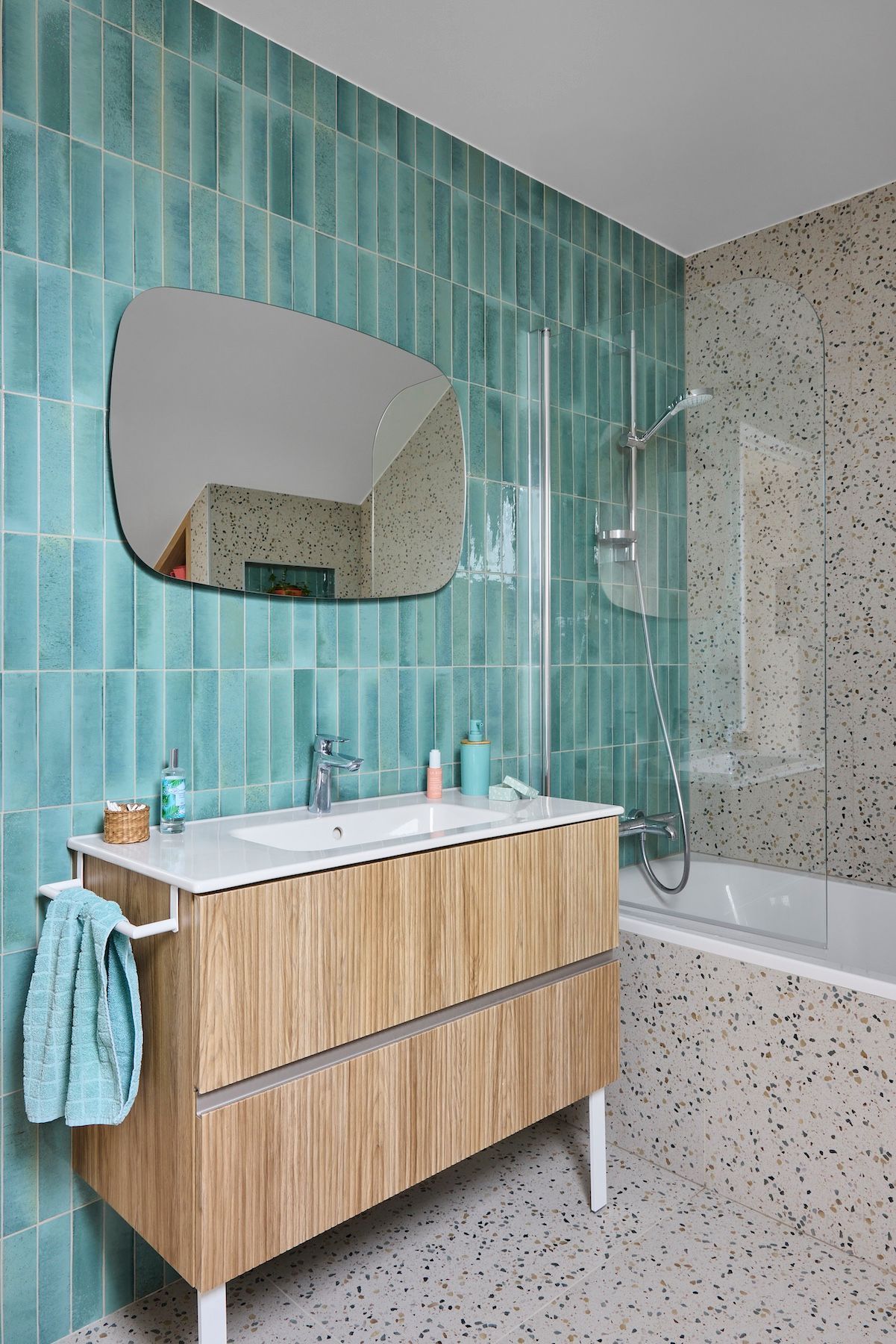 Salle de bains moderne avec mur carrelé bleu turquoise, meuble-lavabo en bois, miroir et baignoire avec douche.