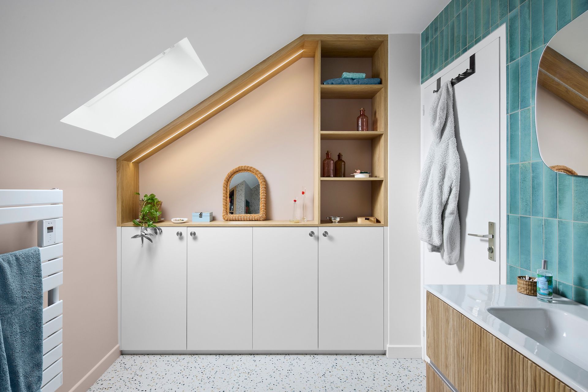 Salle de bain mansardée lumineuse avec plafond en pente, puits de lumière, meubles blancs et douche carrelée turquoise.