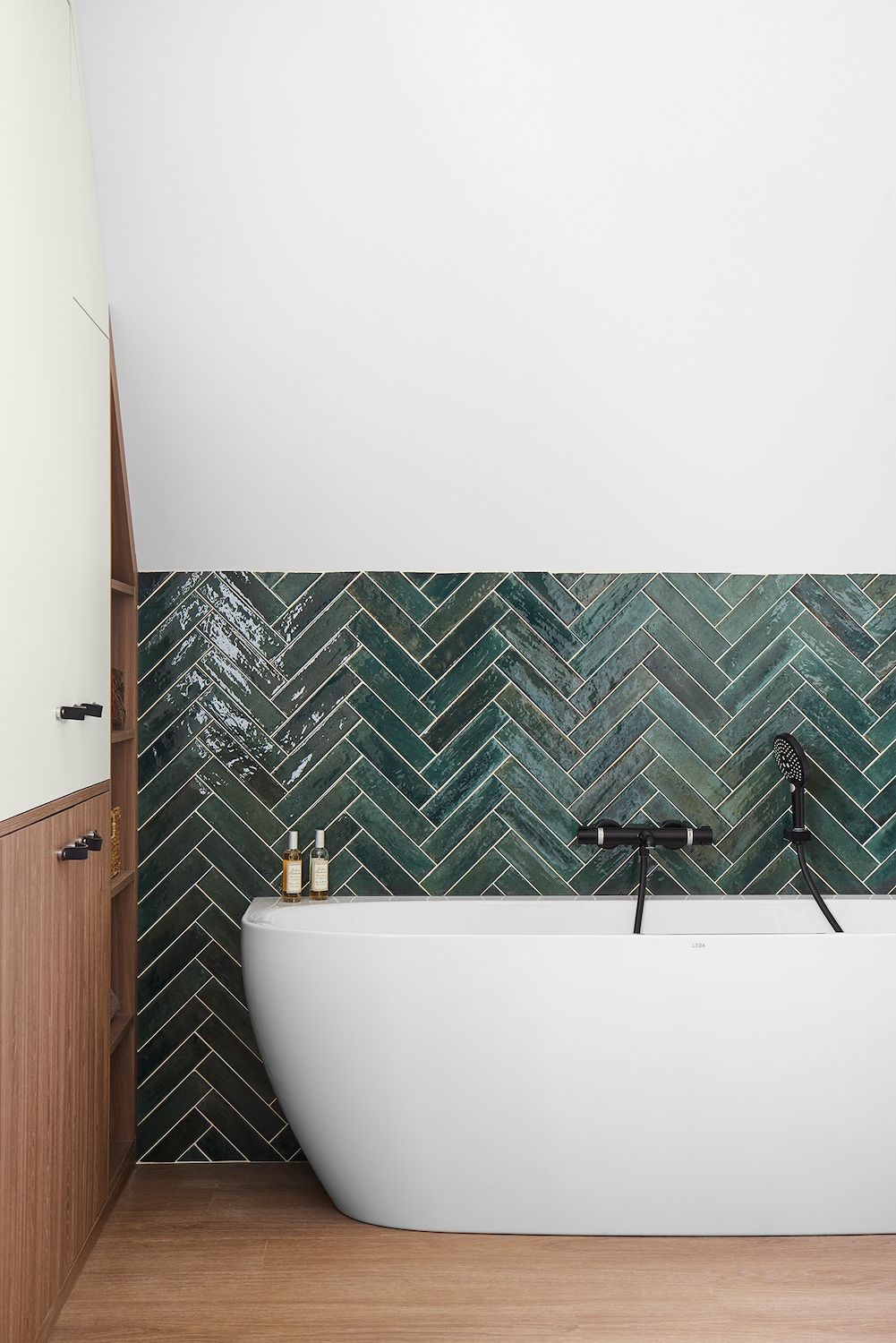 Salle de bains moderne avec baignoire blanche, carrelage à chevrons vert foncé et parquet.
