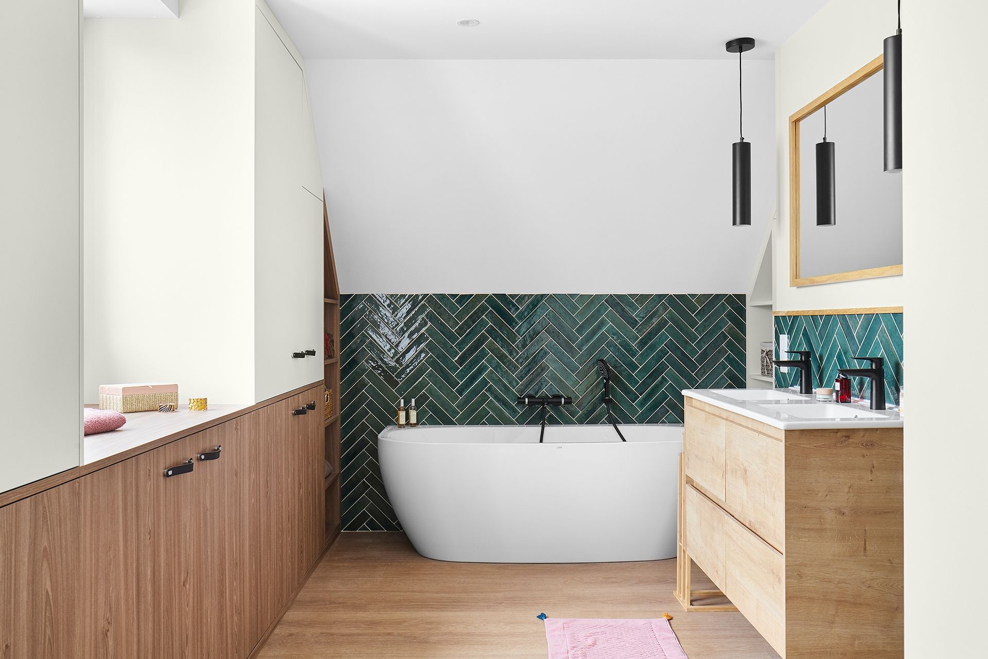 Salle de bains moderne avec baignoire îlot, carrelage vert à chevrons, meuble-lavabo en bois et moulures de puits de lumière.