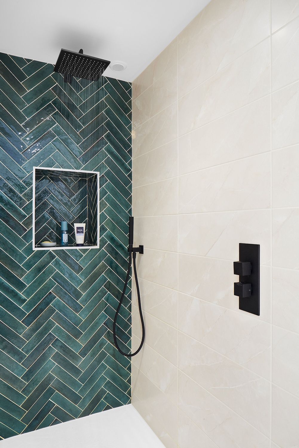Douche moderne avec carrelage vert à chevrons, carrelage mural beige, pommeau de douche effet pluie noir et niche encastrée.