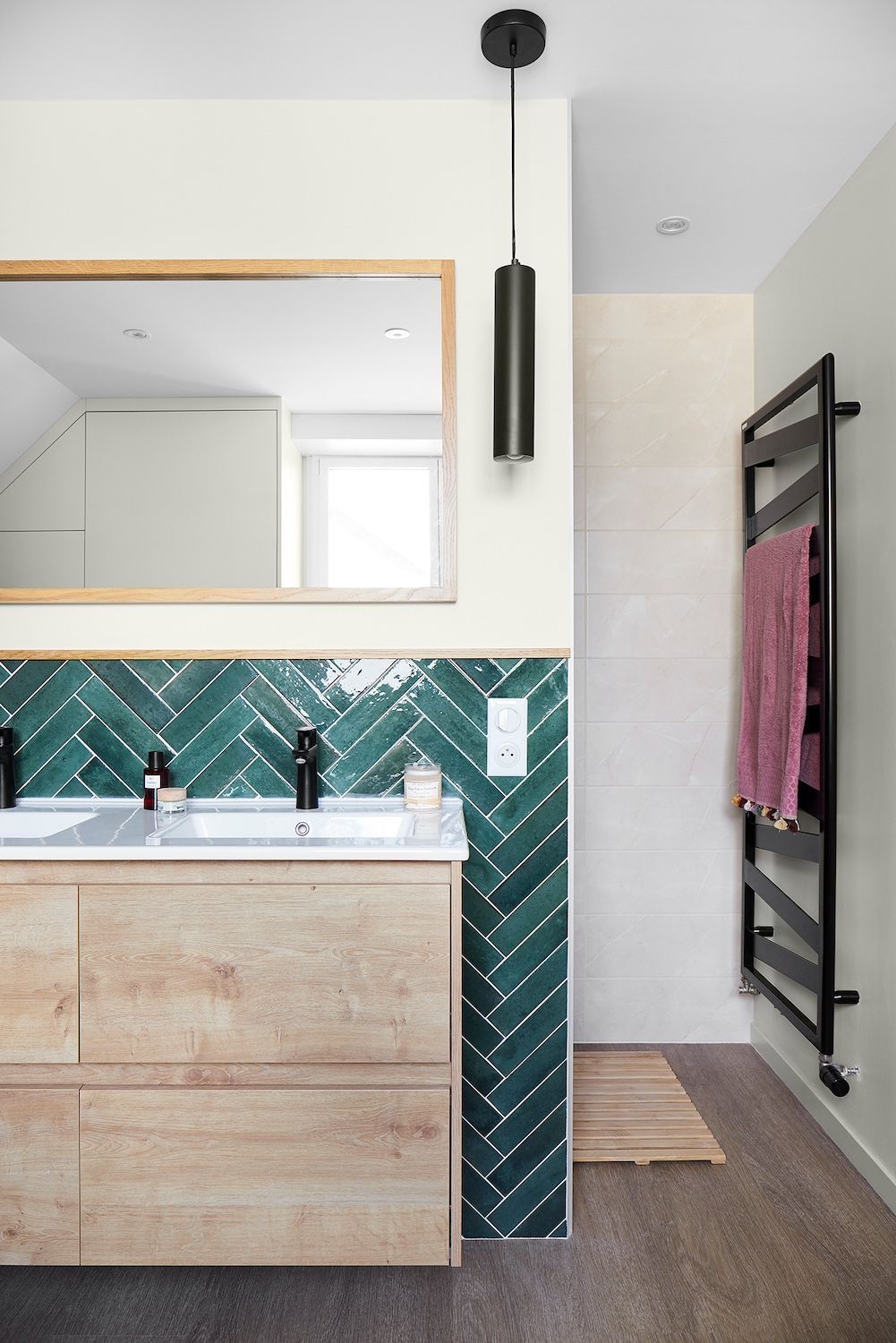 Meuble-lavabo moderne avec armoire en bois, carrelage vert à chevrons, miroir et porte-serviettes chauffant noir.