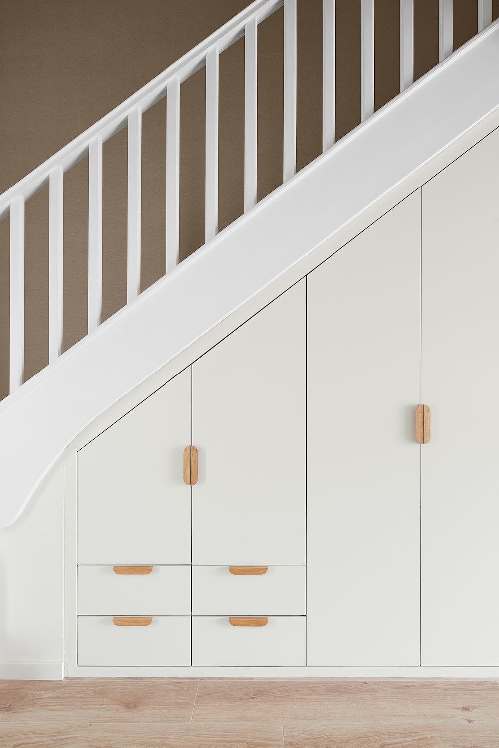 Meuble encastré blanc sous l'escalier avec poignées beiges dans un intérieur minimaliste