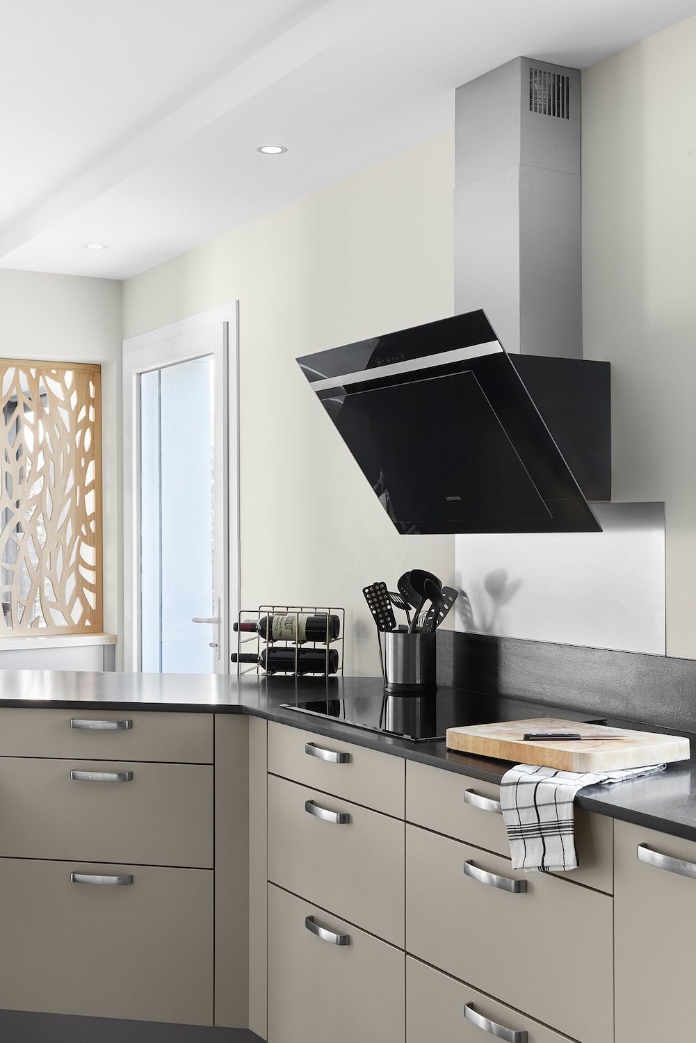 Cuisine moderne avec placards gris, plan de travail noir et hotte aspirante en inox au-dessus de la cuisinière.