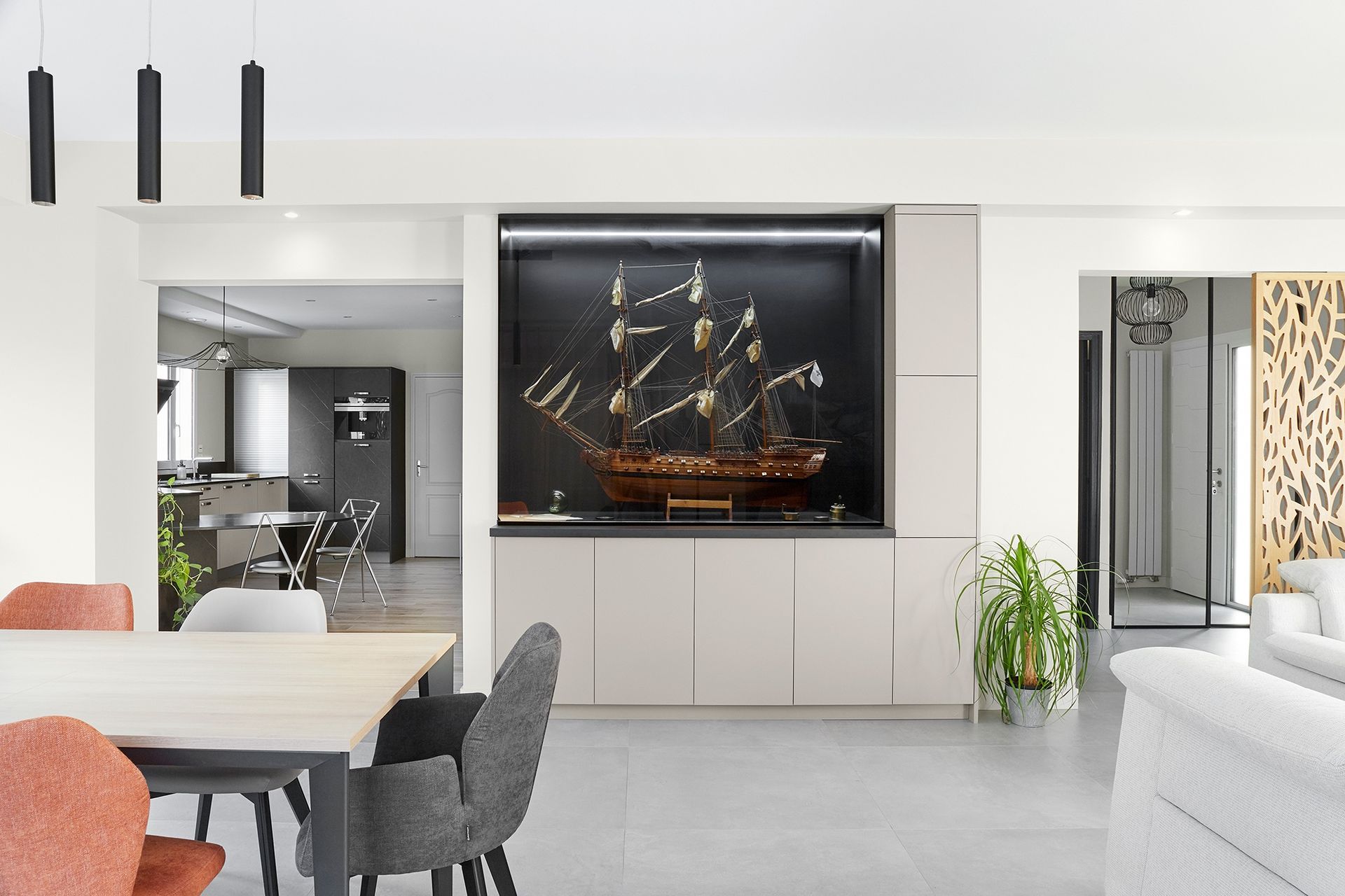 Salle à manger moderne avec chaises noires et vitrine intégrée abritant une maquette de voilier.