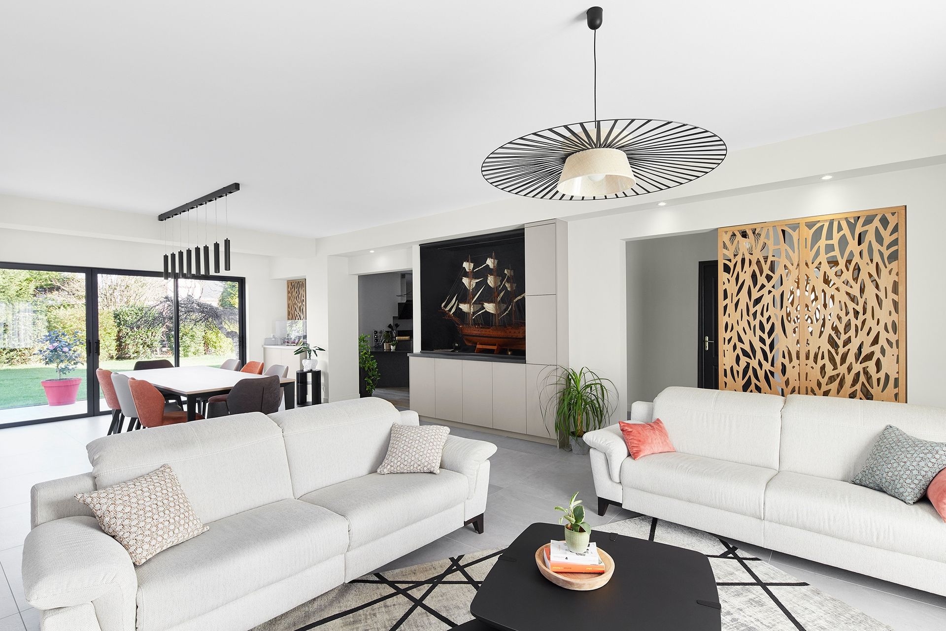 Salon moderne et lumineux avec canapés blancs, table basse noire et coin repas près de grandes fenêtres