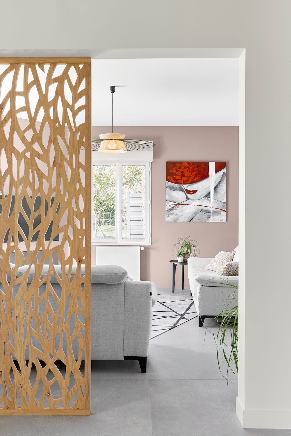 Salon vu à travers un paravent en bois sculpté, avec des sièges gris, des murs roses et des œuvres d'art murales abstraites.
