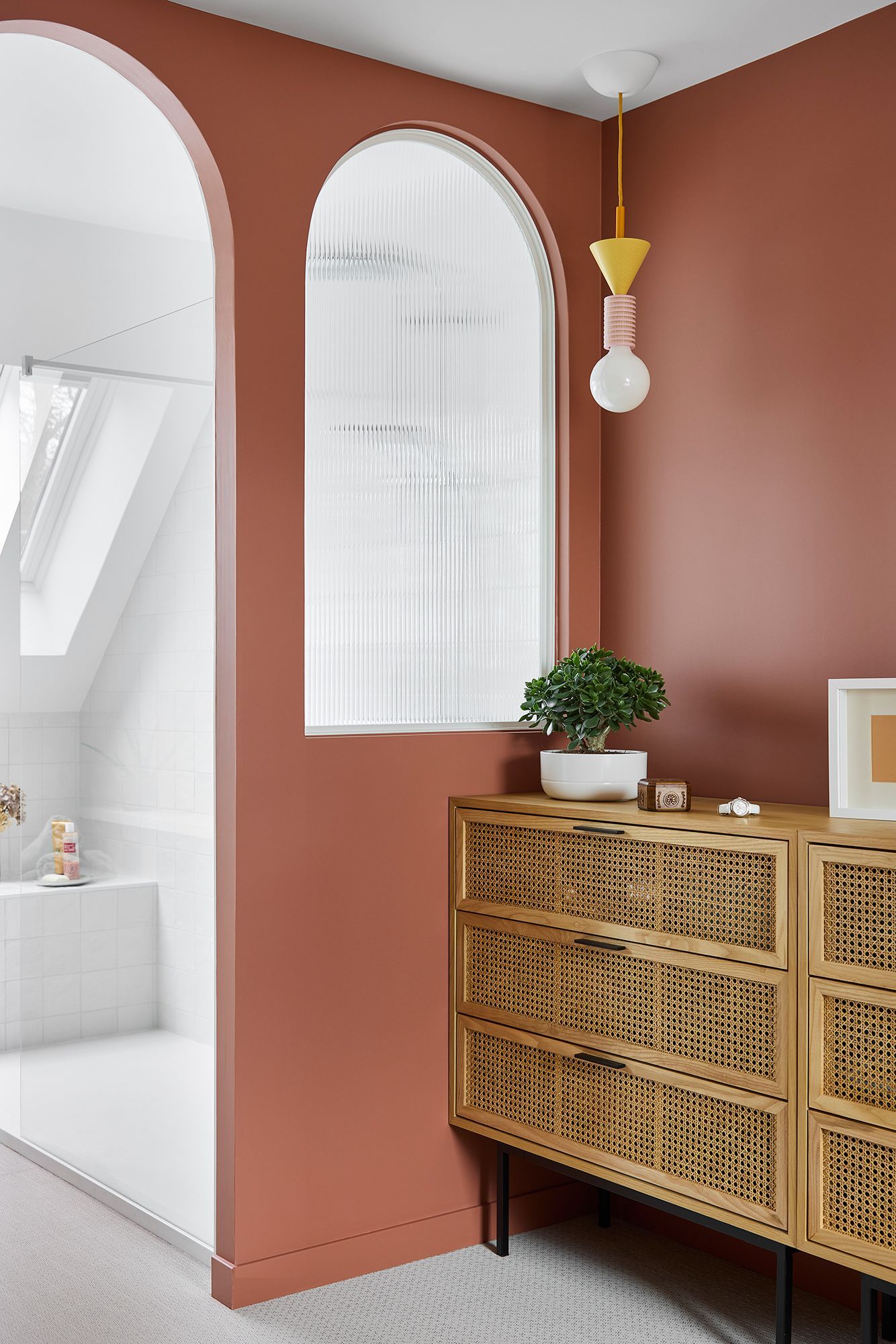Couloir en terre cuite chaleureuse avec porte cintrée, armoire tressée, suspension et petite plante près du mur
