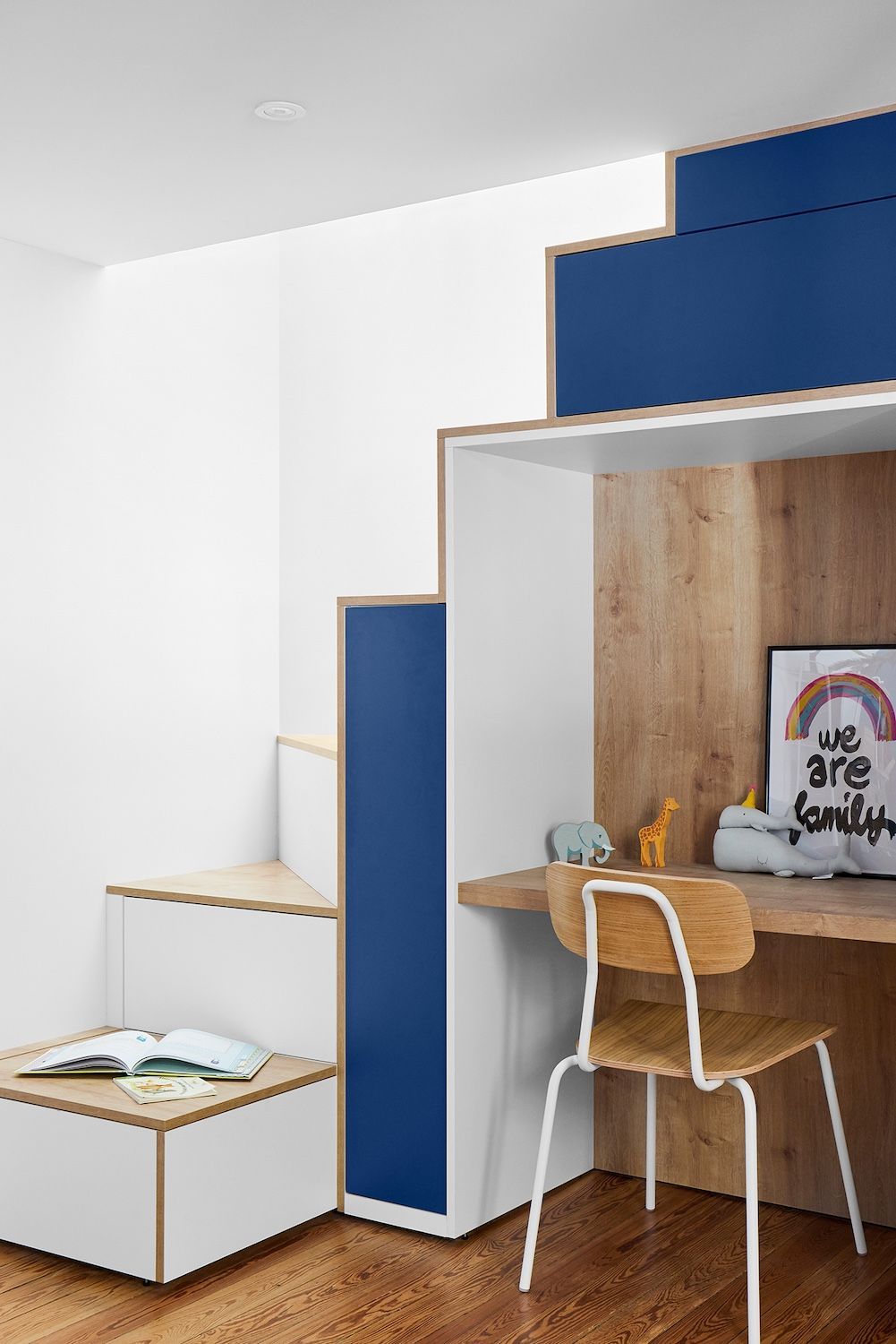 Petit coin mezzanine avec étagères bleues, une chaise de bureau et un lit bas contre un mur blanc