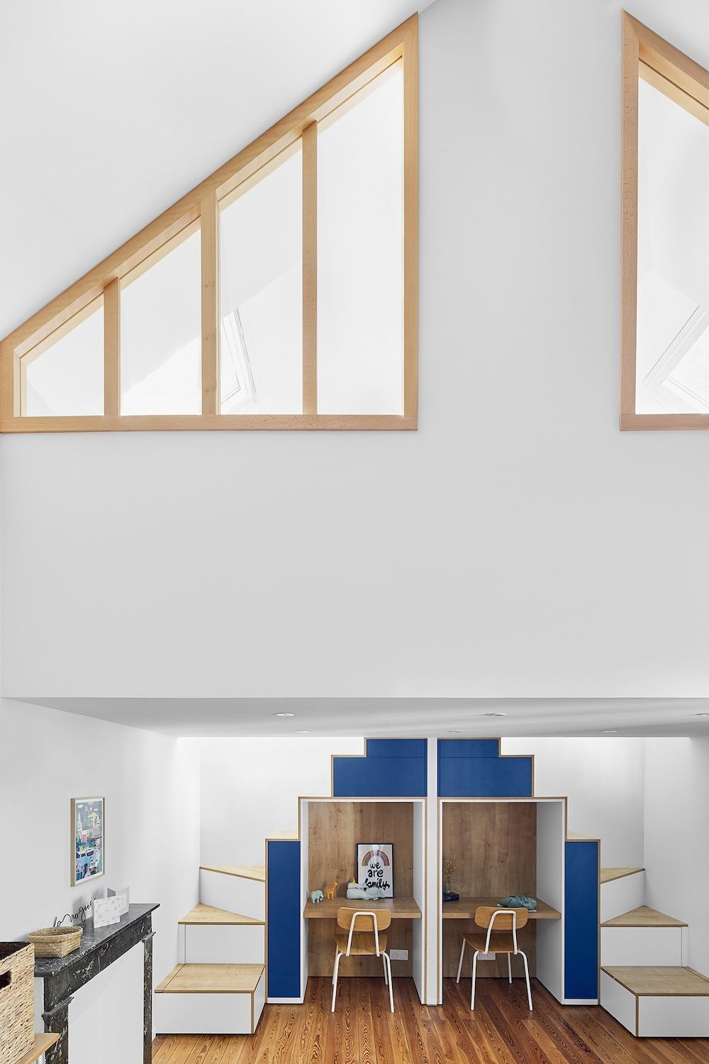 Petite chambre mansardée avec fenêtres en pente, meubles bleus et en bois, et deux chaises autour d'un bureau en contrebas.