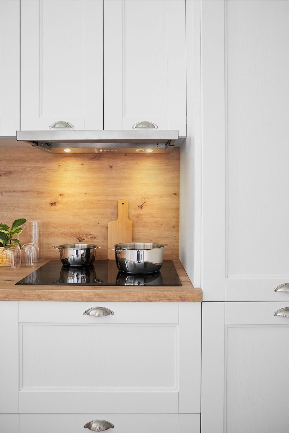 Cuisine blanche avec comptoir en bois, plaque de cuisson encastrée et casseroles en acier inoxydable sous éclairage sous les armoires