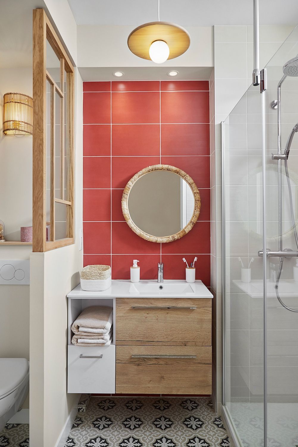 Petite salle de bains avec un mur d'accent en carrelage rouge, un miroir rond, un meuble-lavabo en bois et une douche en verre.