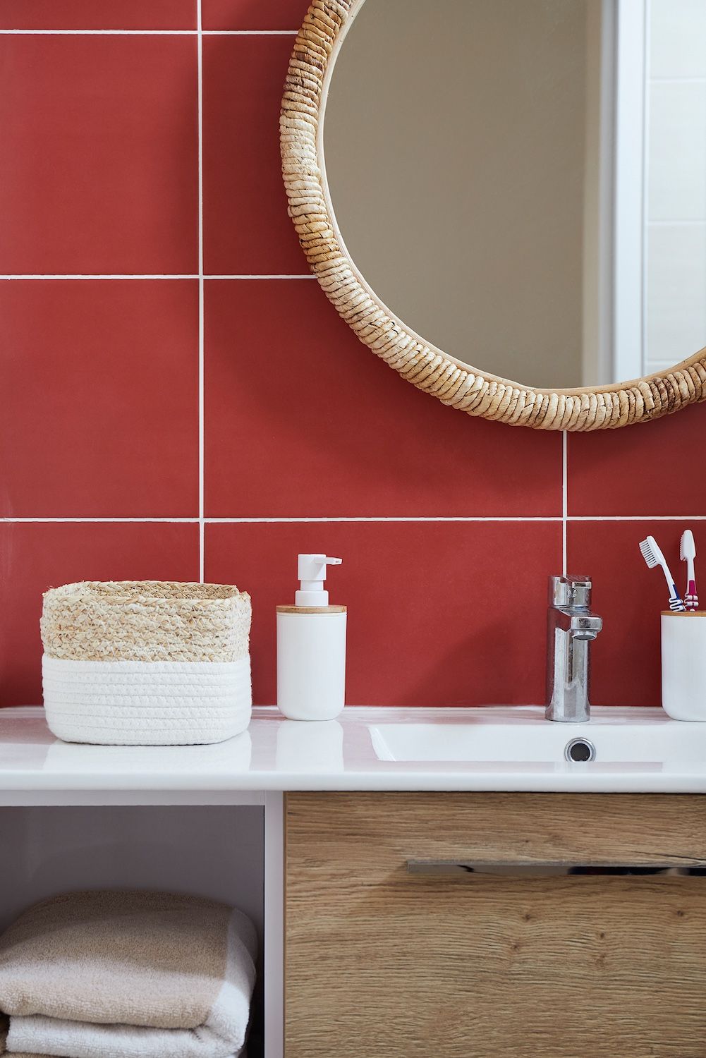 Meuble-lavabo de salle de bain avec mur carrelé de carreaux rouges, miroir rond, comptoir blanc et paniers tressés.