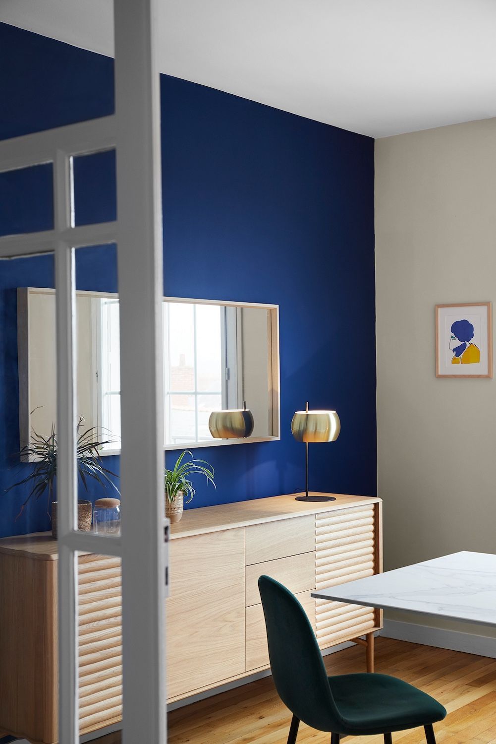 Salle à manger moderne avec un mur d'accent bleu, un buffet, un miroir, une chaise verte et des tableaux encadrés