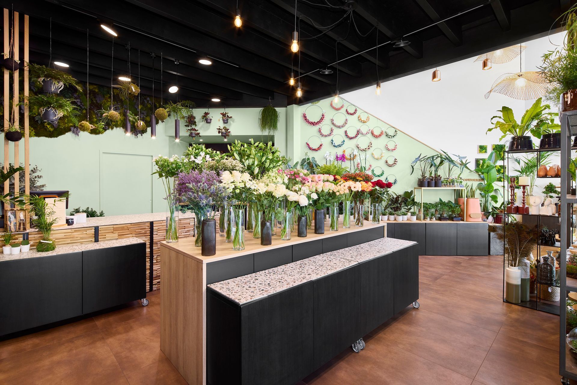 Intérieur d'une boutique de fleurs avec des plantes en pot et des bouquets présentés sur des tables noires et en bois.
