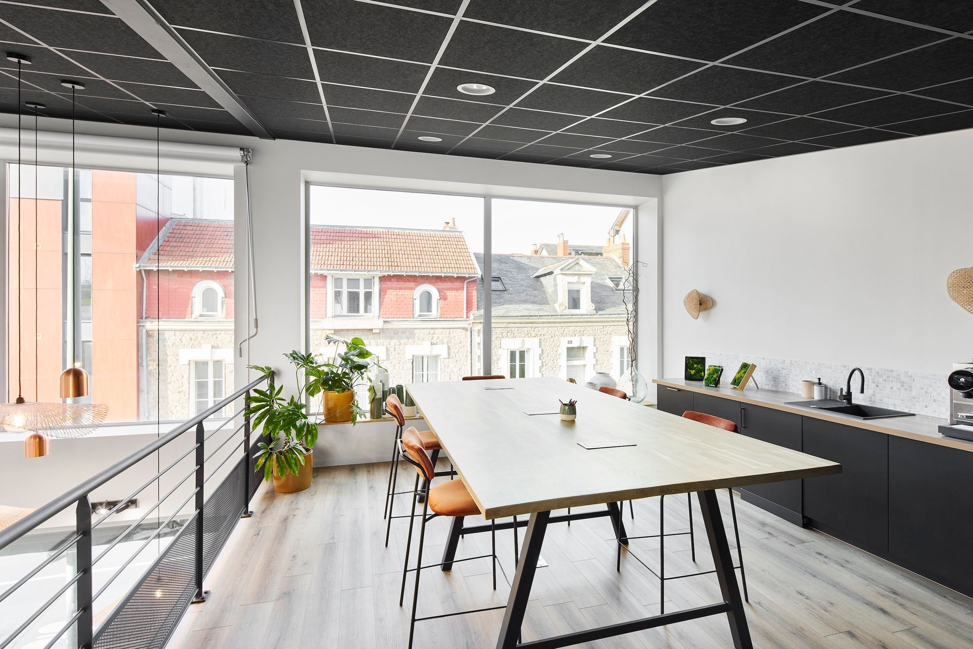 Bureau moderne et lumineux avec de grandes fenêtres, un plafond noir, des murs blancs et une table en bois près de plantes.