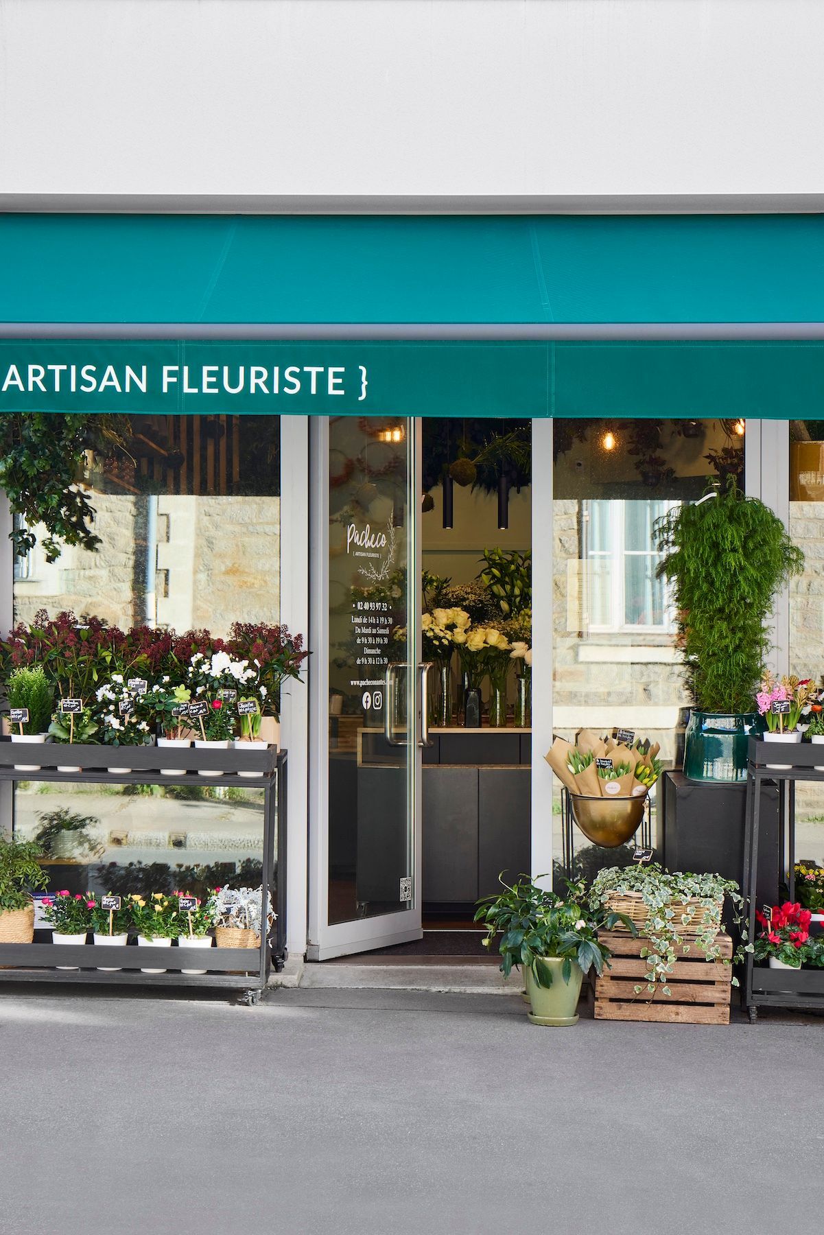 Façade de fleuriste avec auvent turquoise, porte ouverte et plantes en pot à l'extérieur