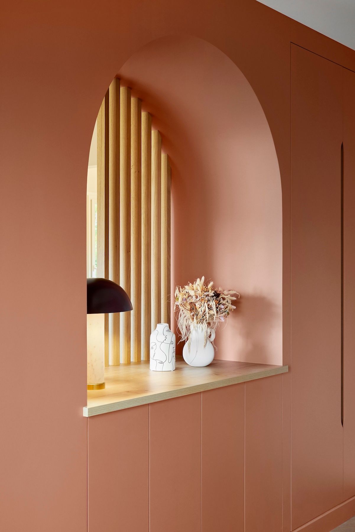 Niche cintrée rose intégrée avec fond à lattes dorées, étagère décorative et mur lambrissé environnant