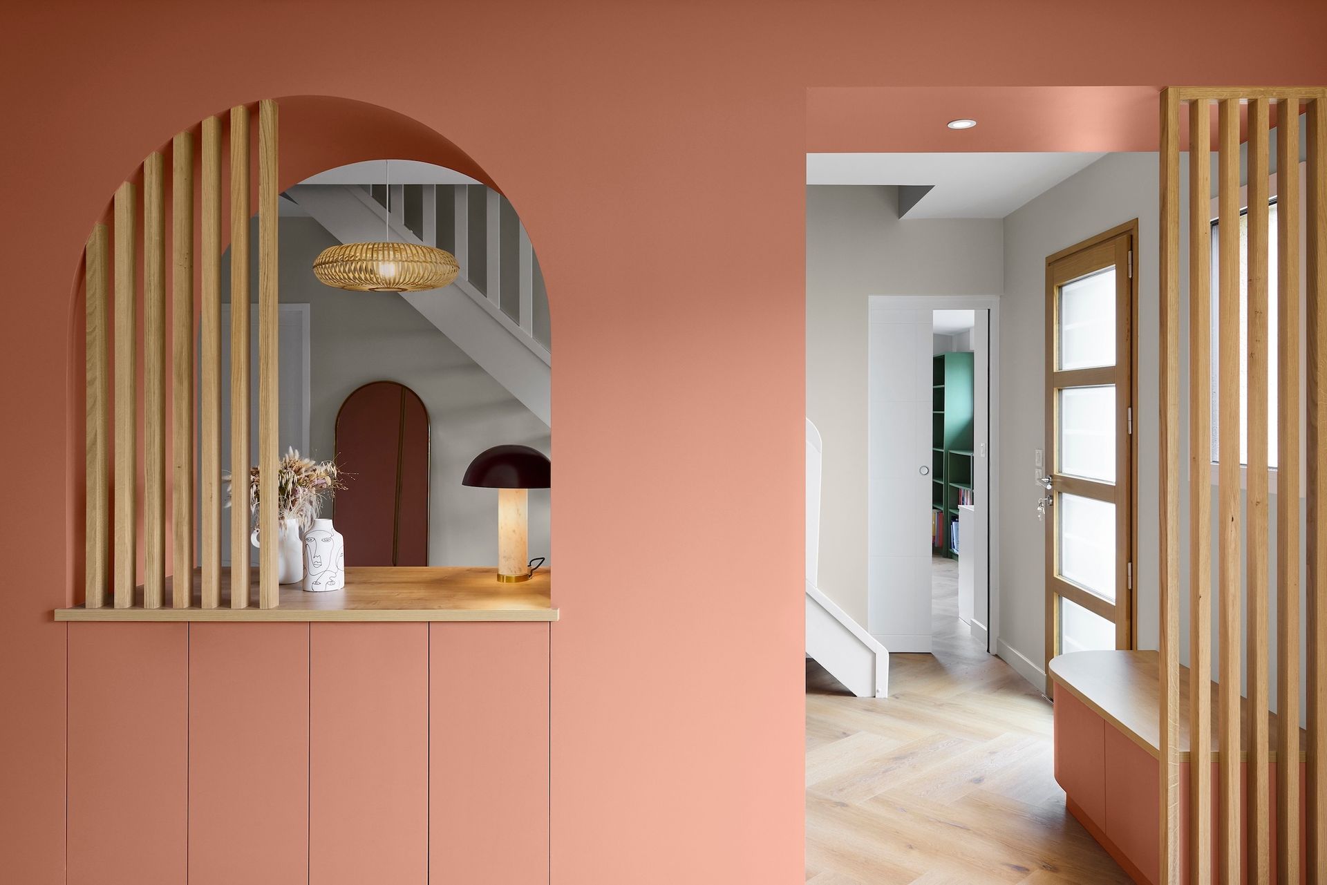 Intérieur rose avec une ouverture de fenêtre cintrée, des lattes de bois et un couloir avec escalier et fenêtres.