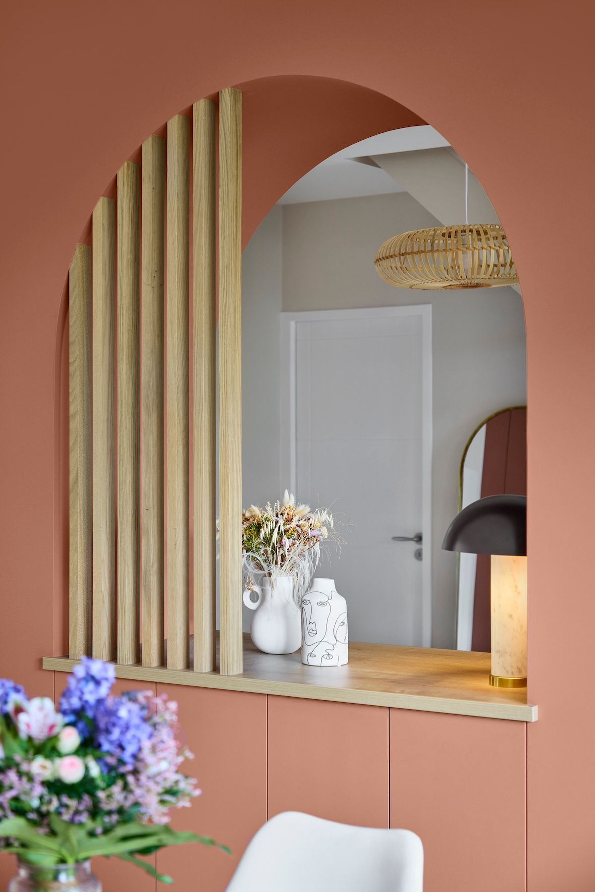 Miroir mural arqué au-dessus d'une coiffeuse pêche, avec des fleurs et une chaise blanche dans une pièce rose pâle