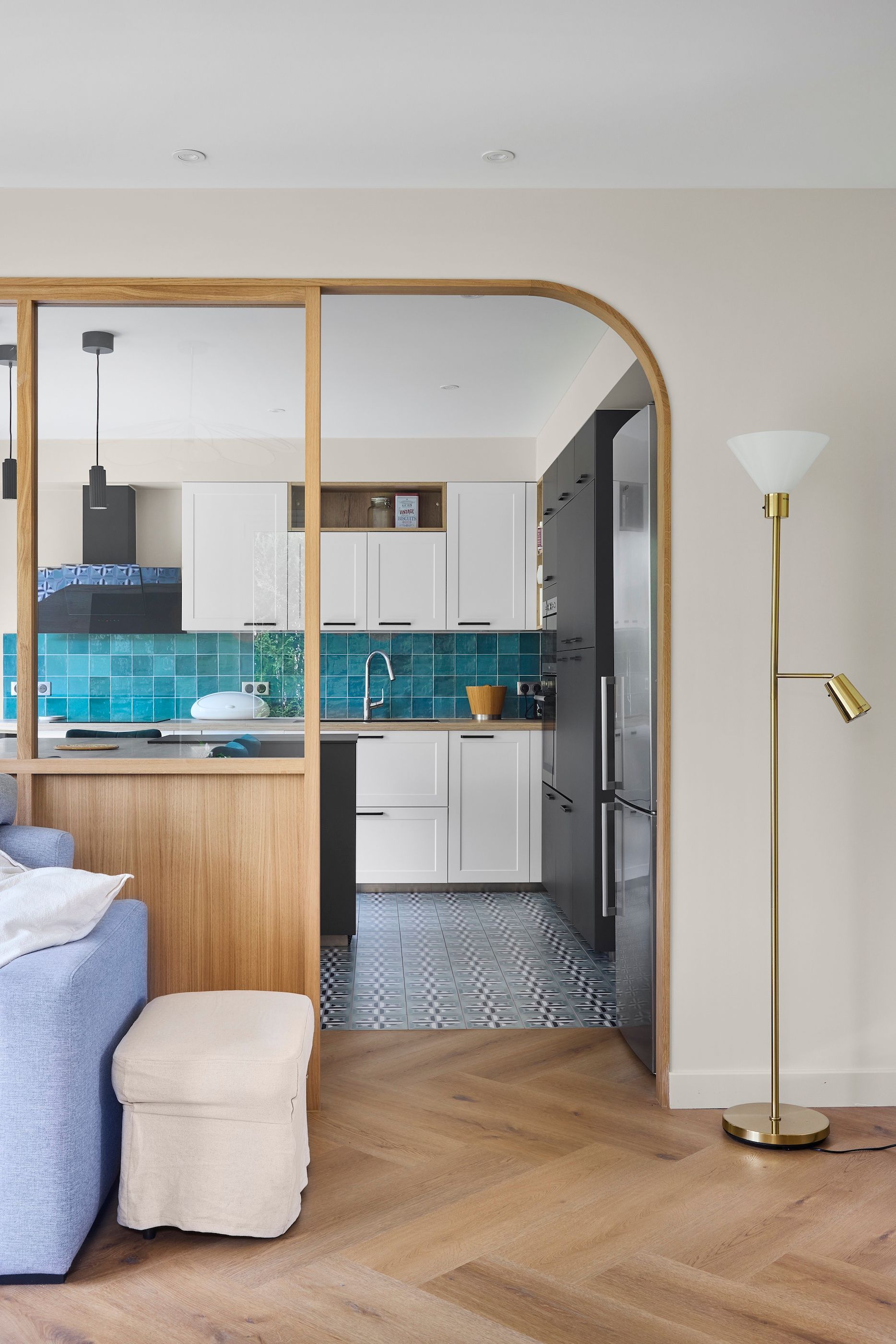 Chambre moderne avec un lit bleu, un lampadaire et une cloison ouverte donnant sur une kitchenette carrelée turquoise