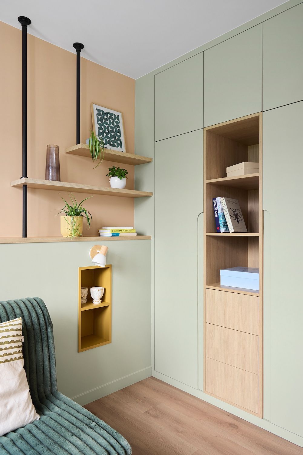 Un coin cosy avec des placards intégrés vert pâle, des étagères en bois, des livres et un petit fauteuil rembourré.