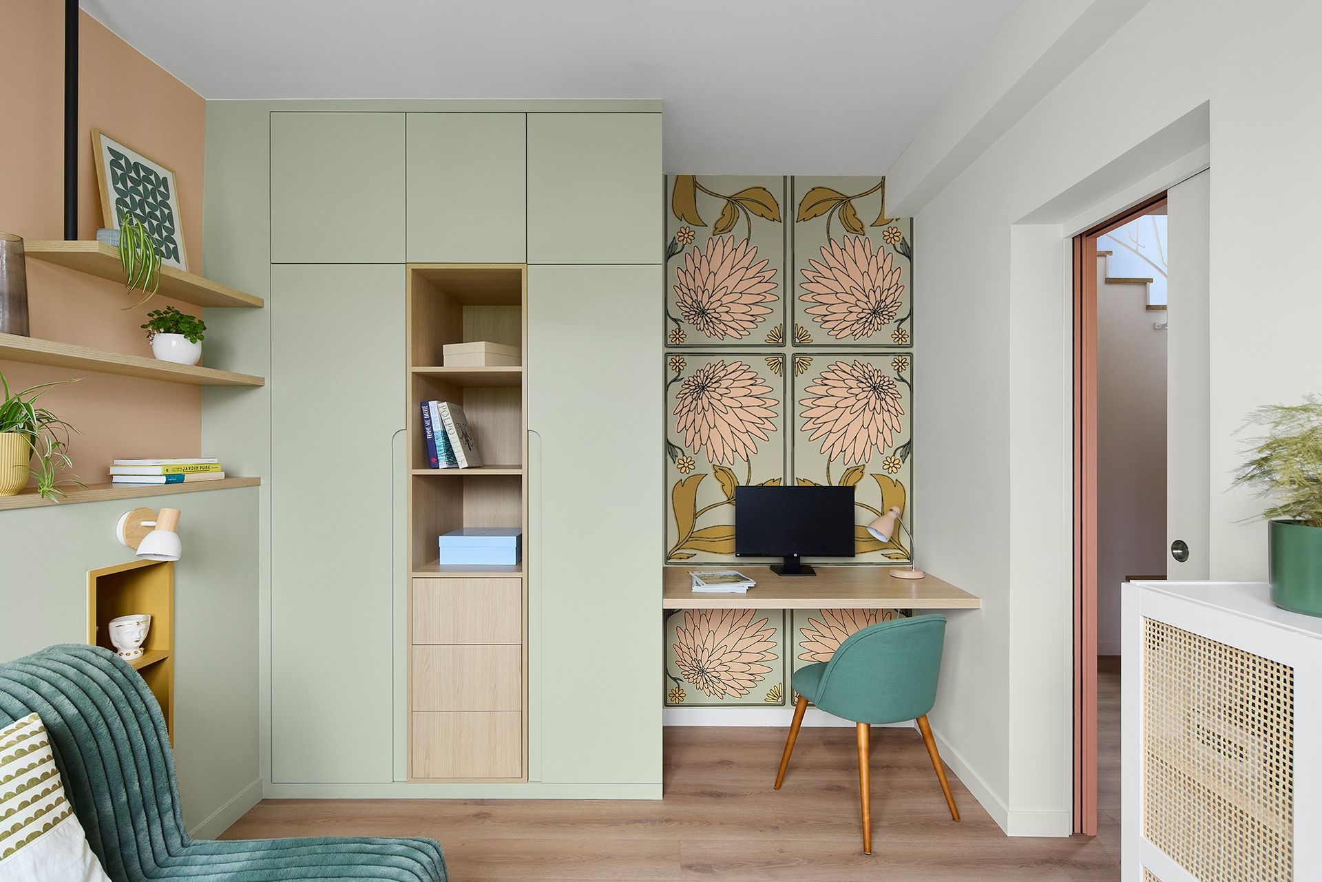 Petit bureau à domicile avec bureau intégré, placards vert menthe, papier peint à motifs et chaise turquoise.