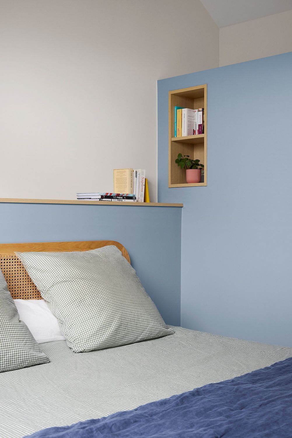 Coin douillet dans la chambre avec mur bleu, lit, étagères, livres et petite niche pour plantes